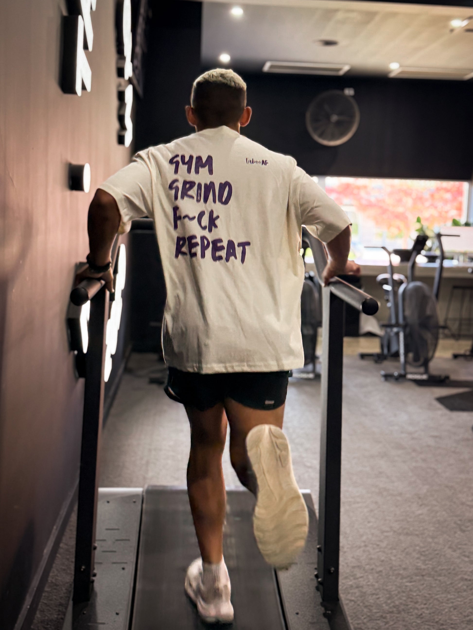 Person walking on a treadmill in a gym with motivational text on their shirt.