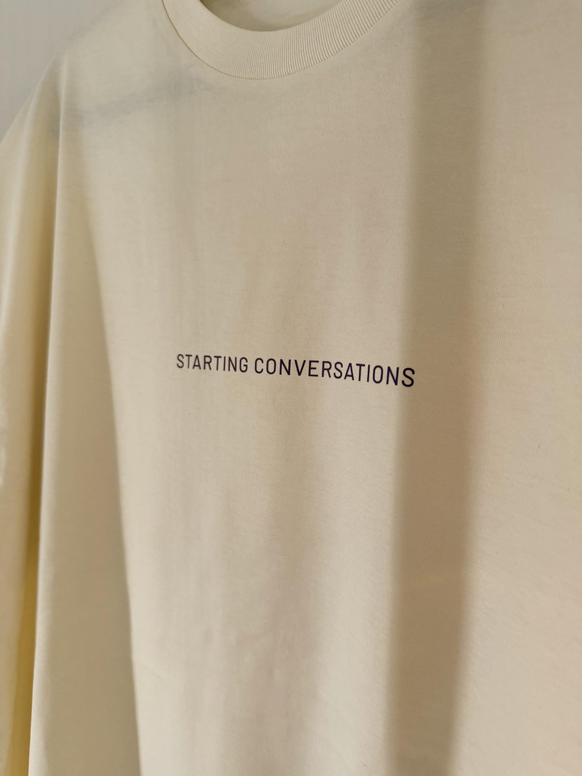 Beige sweatshirt with 'STARTING CONVERSATIONS' text on the front.
