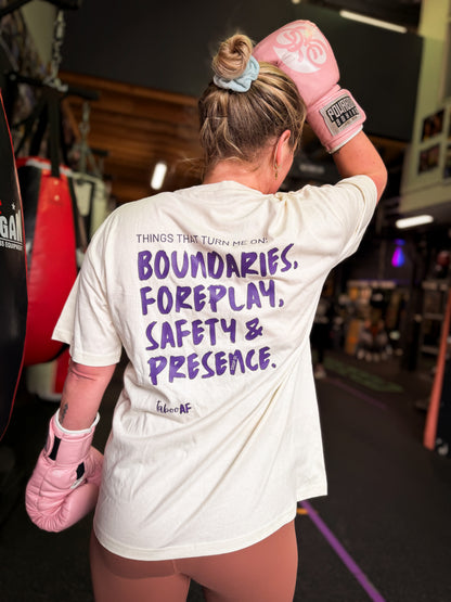 Person in a gym wearing a white t-shirt with text saying Thing that turn me on: Boundaries, Foreplay, Safety & Presence.